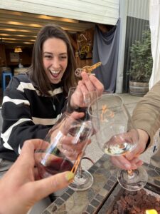 Three wine glasses clinking over the fire at Eleven Winery with Carli, our ED, smiling and holding keys